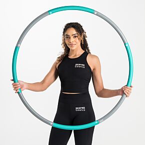 Lady sitting cross-legged on the floor, holding a teal Core Balance 1kg smooth weighted hula hoop in front of her.
